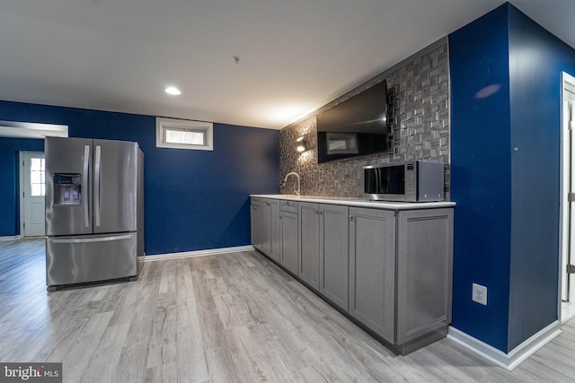 kitchen with baseboards, gray cabinets, light wood-style floors, stainless steel appliances, and a sink