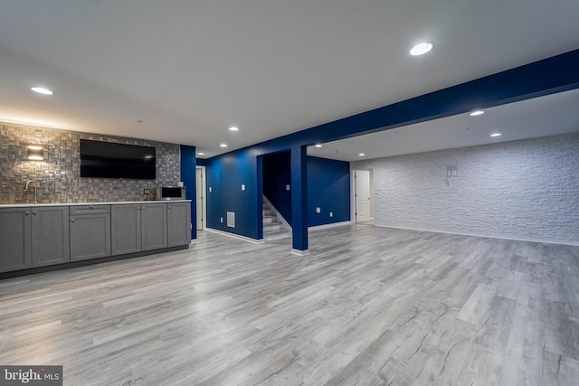 unfurnished living room with recessed lighting, light wood-type flooring, a sink, and stairway