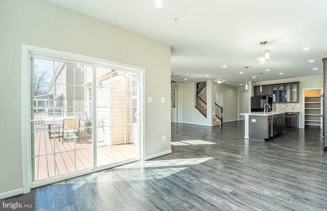 unfurnished living room with stairway, dark wood-style floors, baseboards, ceiling fan, and a sink