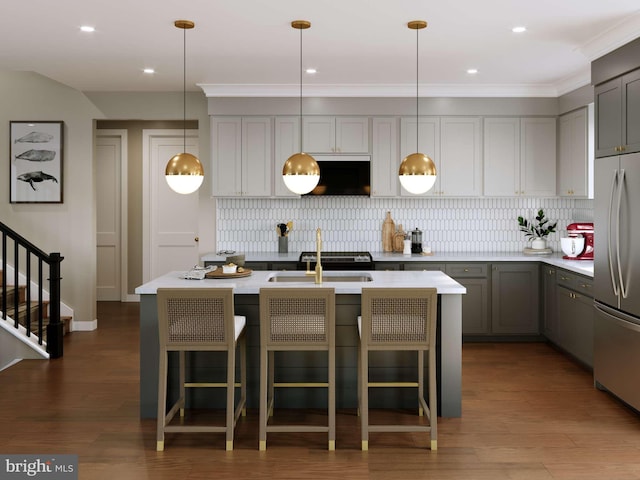 kitchen featuring gray cabinetry, wood finished floors, light countertops, stainless steel refrigerator, and an island with sink