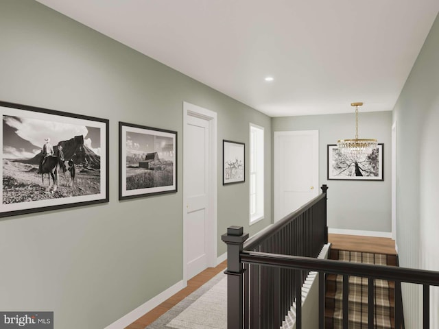 corridor with an inviting chandelier, baseboards, an upstairs landing, and wood finished floors