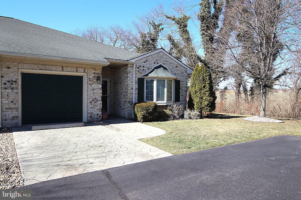 view of front of house with driveway, a front lawn, an attached garage, and a shingled roof