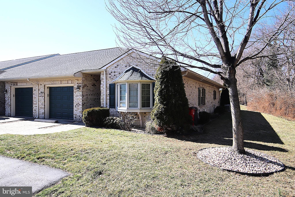 view of front of house with a garage, a shingled roof, a front lawn, and brick siding