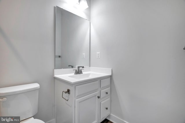 half bath featuring vanity, toilet, and baseboards