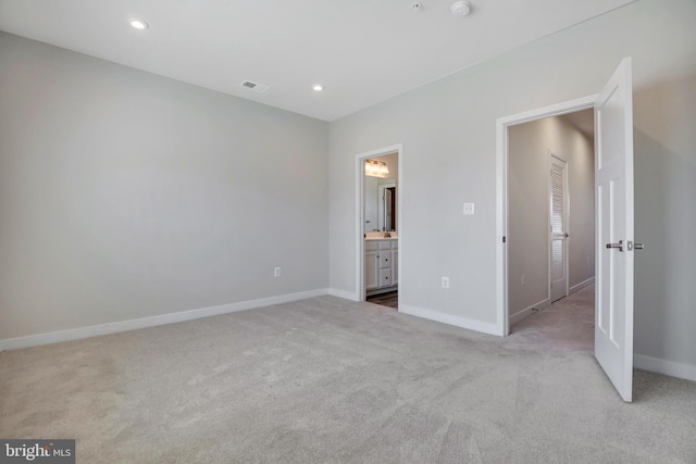 unfurnished bedroom with ensuite bath, recessed lighting, light colored carpet, and baseboards