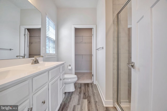 bathroom featuring wood finished floors, a stall shower, a sink, a spacious closet, and toilet