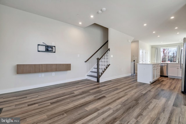 unfurnished living room with recessed lighting, baseboards, wood finished floors, and stairs