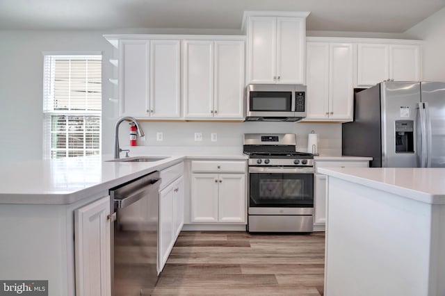 kitchen featuring a sink, white cabinetry, stainless steel appliances, light wood-style floors, and light countertops