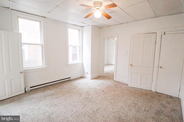 unfurnished bedroom featuring baseboards, a drop ceiling, ceiling fan, carpet flooring, and a baseboard heating unit