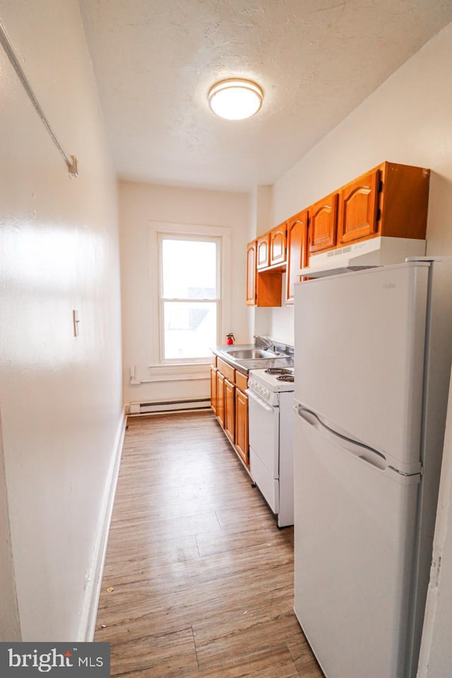 kitchen featuring white appliances, light wood-style flooring, baseboard heating, a textured ceiling, and a sink