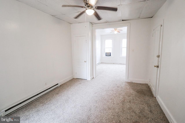 carpeted empty room featuring a baseboard radiator, baseboards, and a drop ceiling