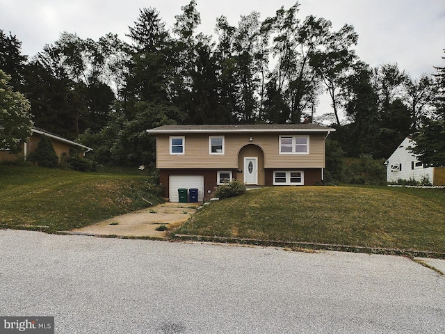 raised ranch featuring driveway, brick siding, a garage, and a front yard