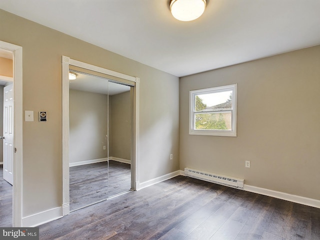 unfurnished bedroom featuring a baseboard heating unit, dark wood-style flooring, a closet, and baseboards