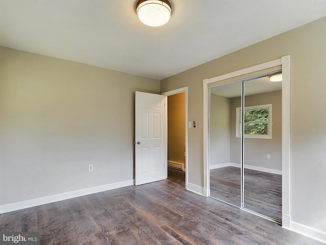 unfurnished bedroom featuring dark wood-type flooring, a closet, a baseboard radiator, and baseboards