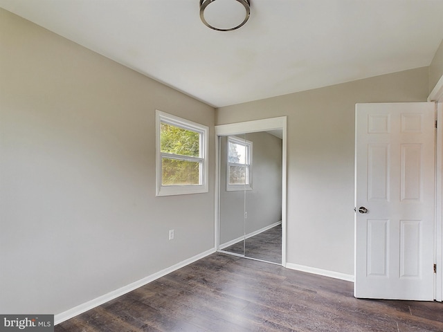 unfurnished bedroom featuring dark wood-style floors, a closet, and baseboards