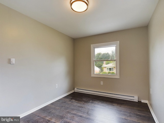 spare room featuring a baseboard heating unit, dark wood-style flooring, and baseboards