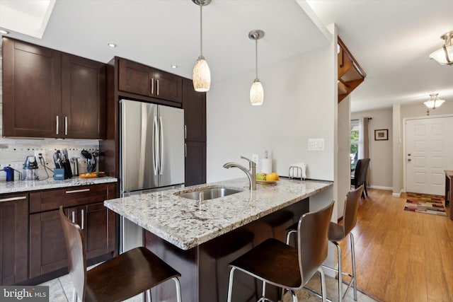 kitchen featuring light wood finished floors, a breakfast bar, freestanding refrigerator, a sink, and backsplash