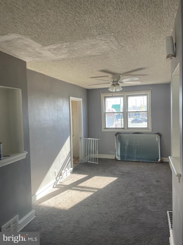 carpeted spare room with a textured ceiling, baseboards, visible vents, and ceiling fan