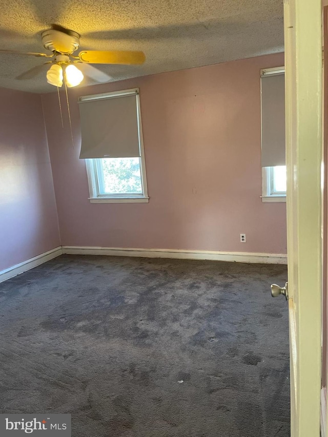 empty room featuring a ceiling fan, baseboards, dark carpet, and a textured ceiling