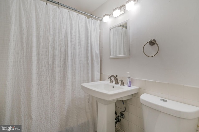 full bath with a wainscoted wall, a shower with curtain, toilet, and tile walls