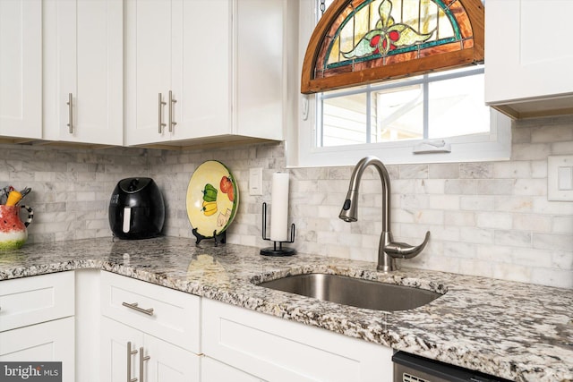 kitchen with a sink, light stone counters, dishwasher, and white cabinetry