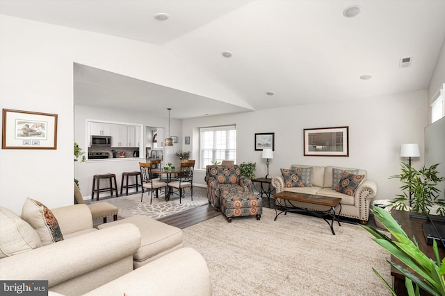 living room featuring visible vents, lofted ceiling, and wood finished floors