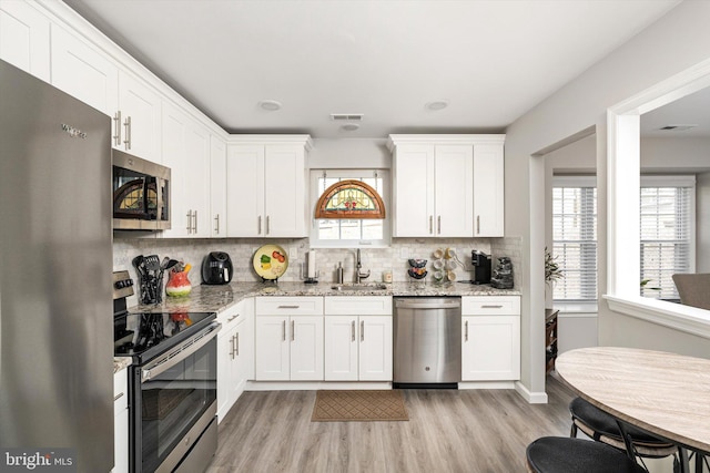 kitchen featuring visible vents, a sink, backsplash, stainless steel appliances, and white cabinets