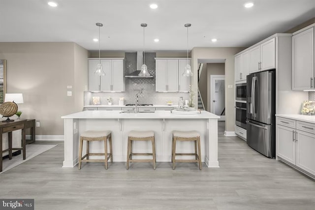 kitchen featuring stainless steel appliances, a breakfast bar area, a center island with sink, and wall chimney exhaust hood