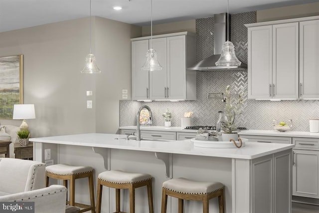 kitchen featuring a breakfast bar, wall chimney exhaust hood, light countertops, and backsplash