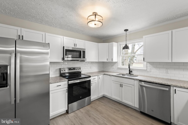 kitchen featuring stainless steel appliances, tasteful backsplash, white cabinetry, a sink, and light wood-type flooring