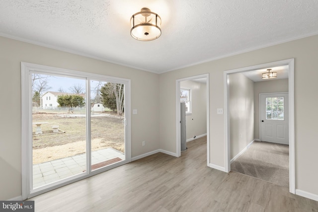 unfurnished dining area featuring a textured ceiling, ornamental molding, light wood-type flooring, and baseboards