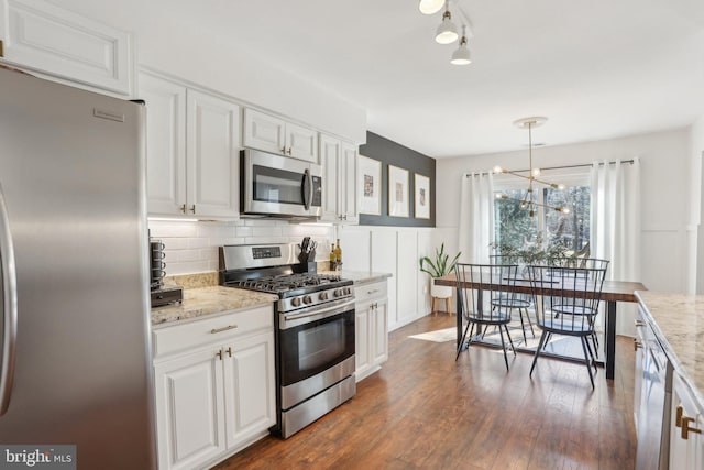 kitchen with white cabinets, dark wood finished floors, appliances with stainless steel finishes, light stone countertops, and backsplash