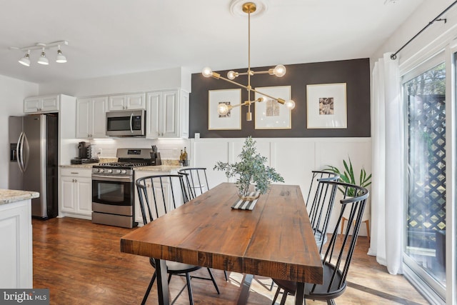 dining area featuring wainscoting, a decorative wall, an inviting chandelier, and wood finished floors