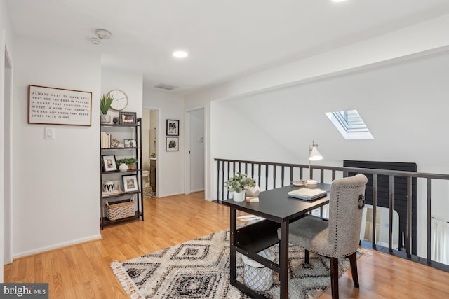 office space with vaulted ceiling with skylight, baseboards, and light wood finished floors