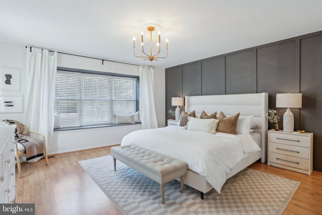 bedroom featuring a chandelier, light wood-style floors, and a decorative wall