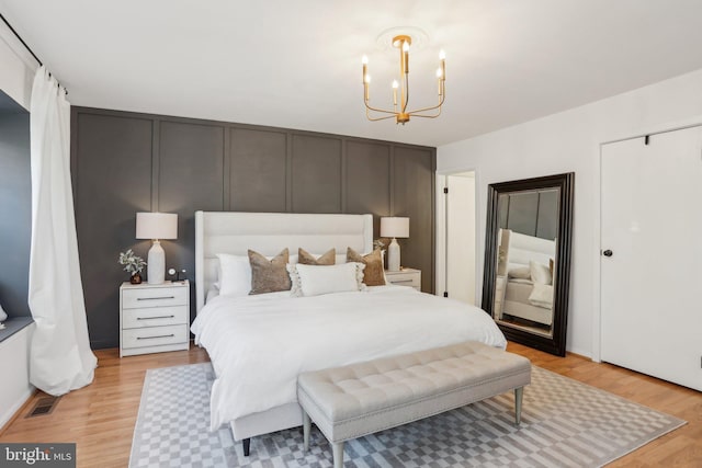 bedroom featuring light wood-type flooring, visible vents, a chandelier, and a decorative wall