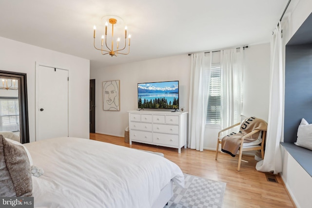 bedroom featuring baseboards, multiple windows, light wood-style flooring, and a notable chandelier