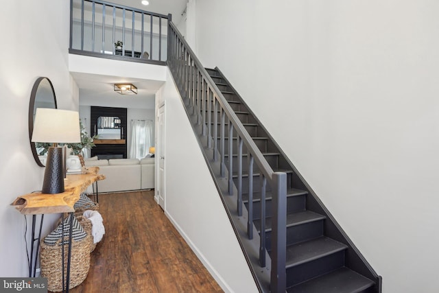 staircase featuring wood finished floors, a towering ceiling, and baseboards