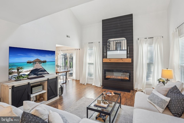 living room featuring high vaulted ceiling, visible vents, a fireplace, and wood finished floors