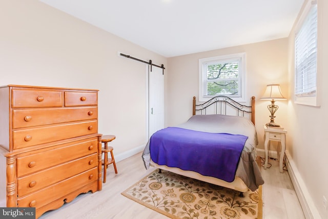bedroom with a baseboard heating unit, a barn door, baseboards, and light wood finished floors