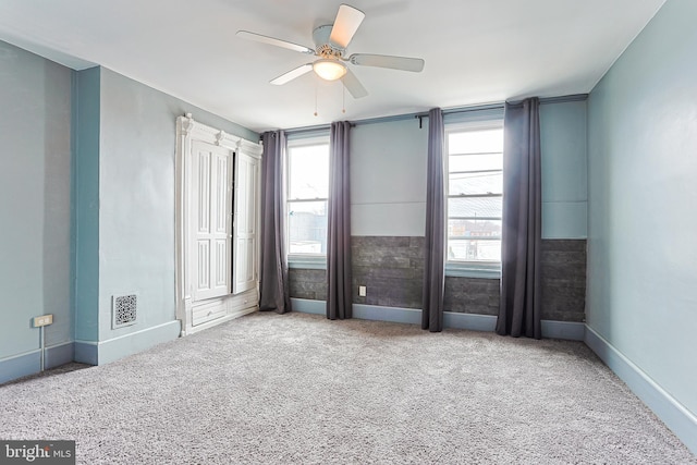 empty room with carpet, ceiling fan, visible vents, and a wealth of natural light