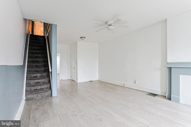 unfurnished living room with a ceiling fan, baseboards, visible vents, light wood-style floors, and stairway