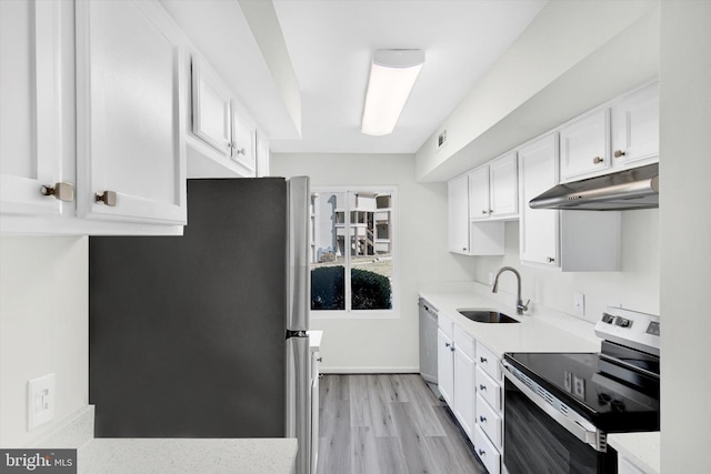 kitchen with under cabinet range hood, a sink, white cabinets, appliances with stainless steel finishes, and light wood finished floors