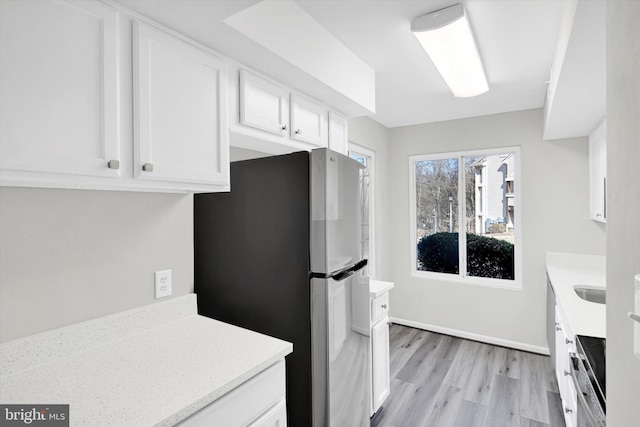 kitchen featuring baseboards, light wood-style floors, freestanding refrigerator, and white cabinets