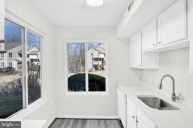 kitchen with baseboards, visible vents, white cabinets, light wood-style floors, and a sink