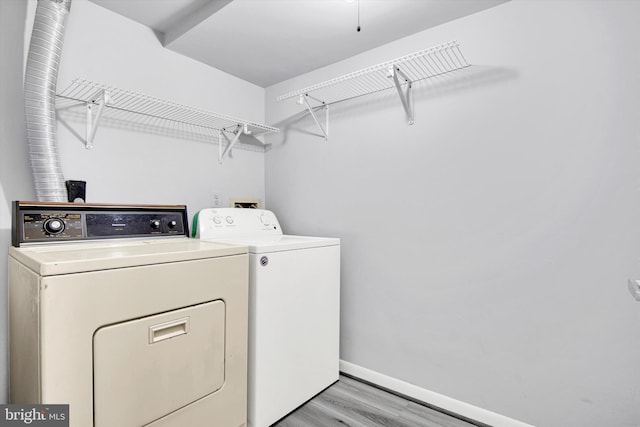 clothes washing area featuring laundry area, separate washer and dryer, light wood-style flooring, and baseboards