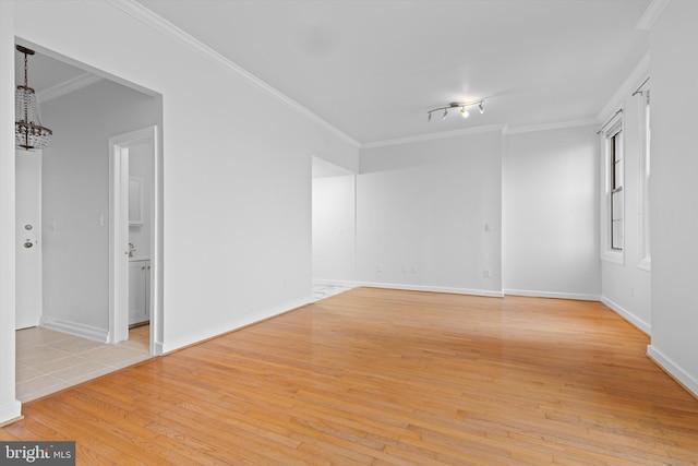 spare room featuring light wood-style floors, a chandelier, crown molding, and baseboards