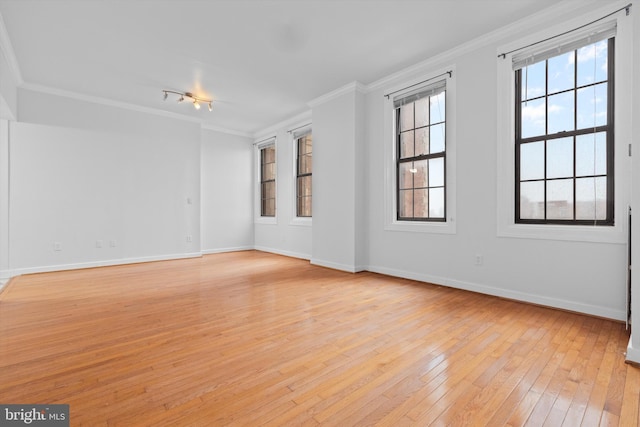 empty room featuring light wood-type flooring, crown molding, and baseboards