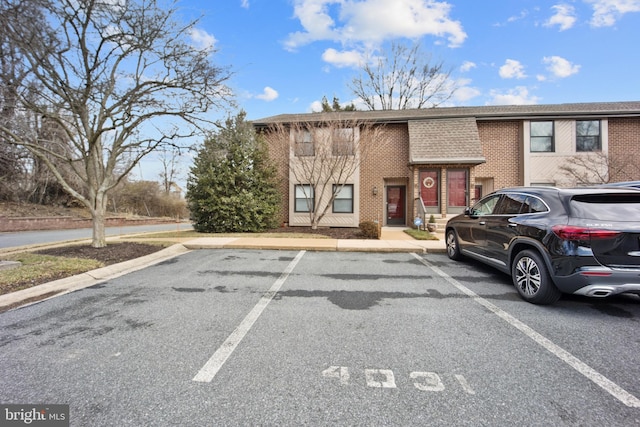 exterior space with roof with shingles, uncovered parking, and brick siding