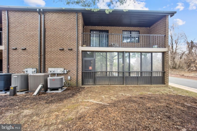 rear view of property with a balcony, central air condition unit, and brick siding